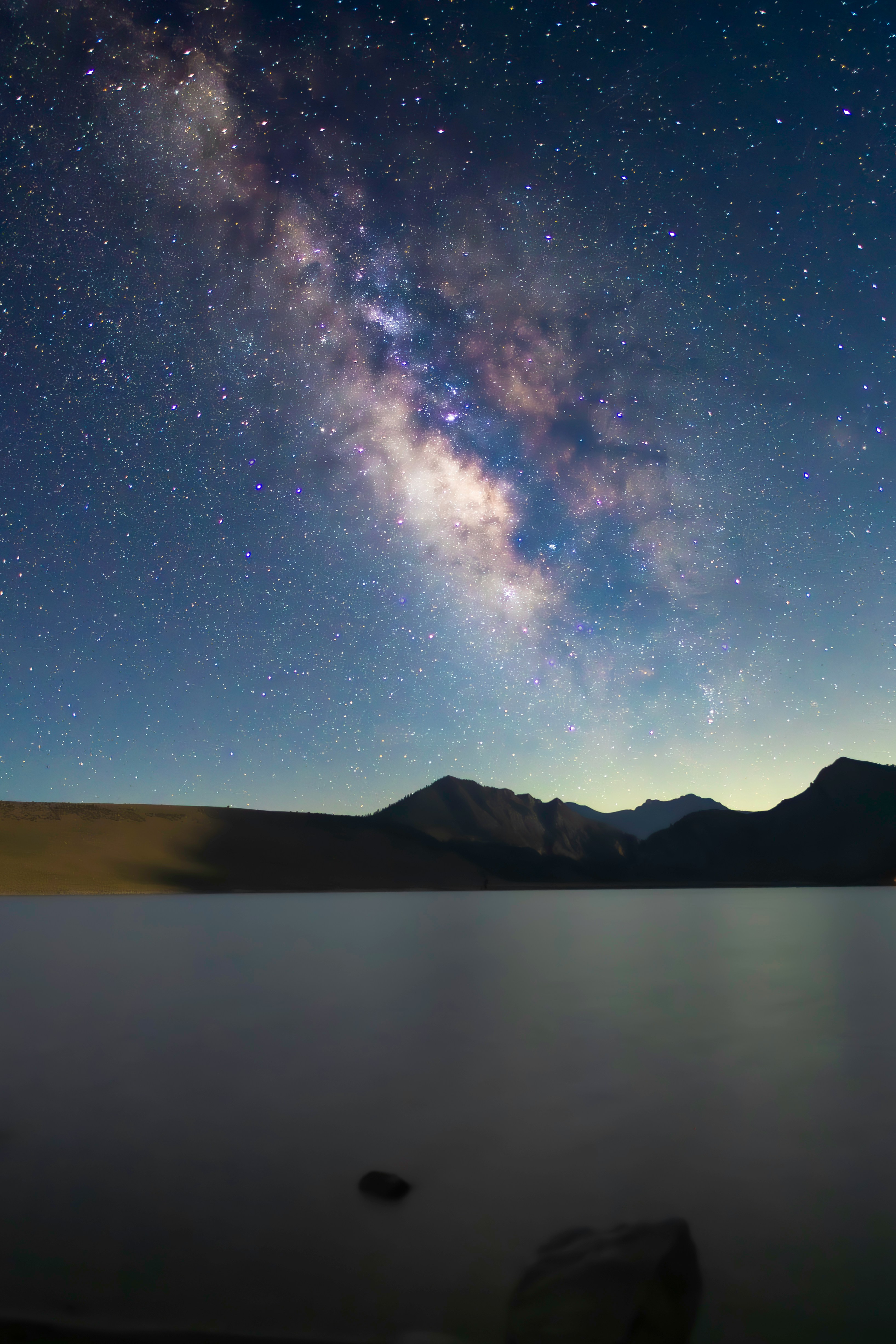 The Milky Way over a still lake and stone bridge
